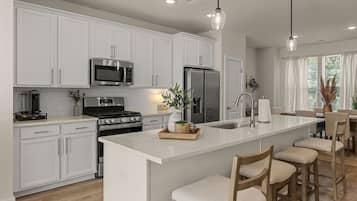 A modern kitchen with white cabinetry, stainless steel appliances, a central island with bar stools, and pendant lighting.