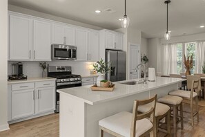 A modern kitchen with white cabinetry, stainless steel appliances, a central island with bar stools, and pendant lighting.