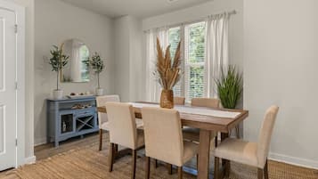 A dining area with a wooden table, six chairs, a blue console, and a large window with curtains.