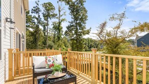 A wooden deck with a sofa and a table, surrounded by a wooden railing. - Lux Charleston Residence for 10+ (Hanahan)