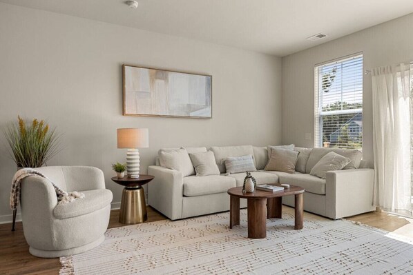 A living room with a sofa, armchair, coffee table, lamp, and artwork on the wall.