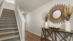 A staircase leading to a door, a wooden console table with a mirror and vases, and a wall-mounted sunburst mirror. - Lux Charleston Residence for 10+ (Hanahan)