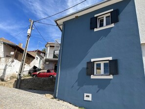 A residential building with a blue exterior, two windows with shutters, and a red car parked in front.
