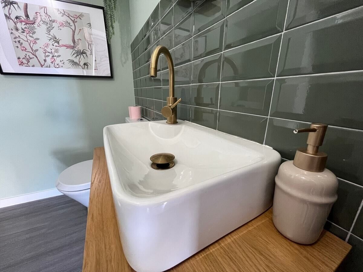 A bathroom with a white sink, a gold faucet, and a soap dispenser.