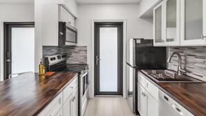 Eine moderne Küche mit weißen Schränken, einer Holz Arbeitsplatte, einer eingebauten Mikrowelle, einem Edelstahl-Kühlschrank und einer schwarzen Kochplatte.