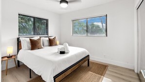 Ein Schlafzimmer mit einem Bett, zwei Nachttischen, einem Deckenventilator und zwei Fenstern mit Jalousien.