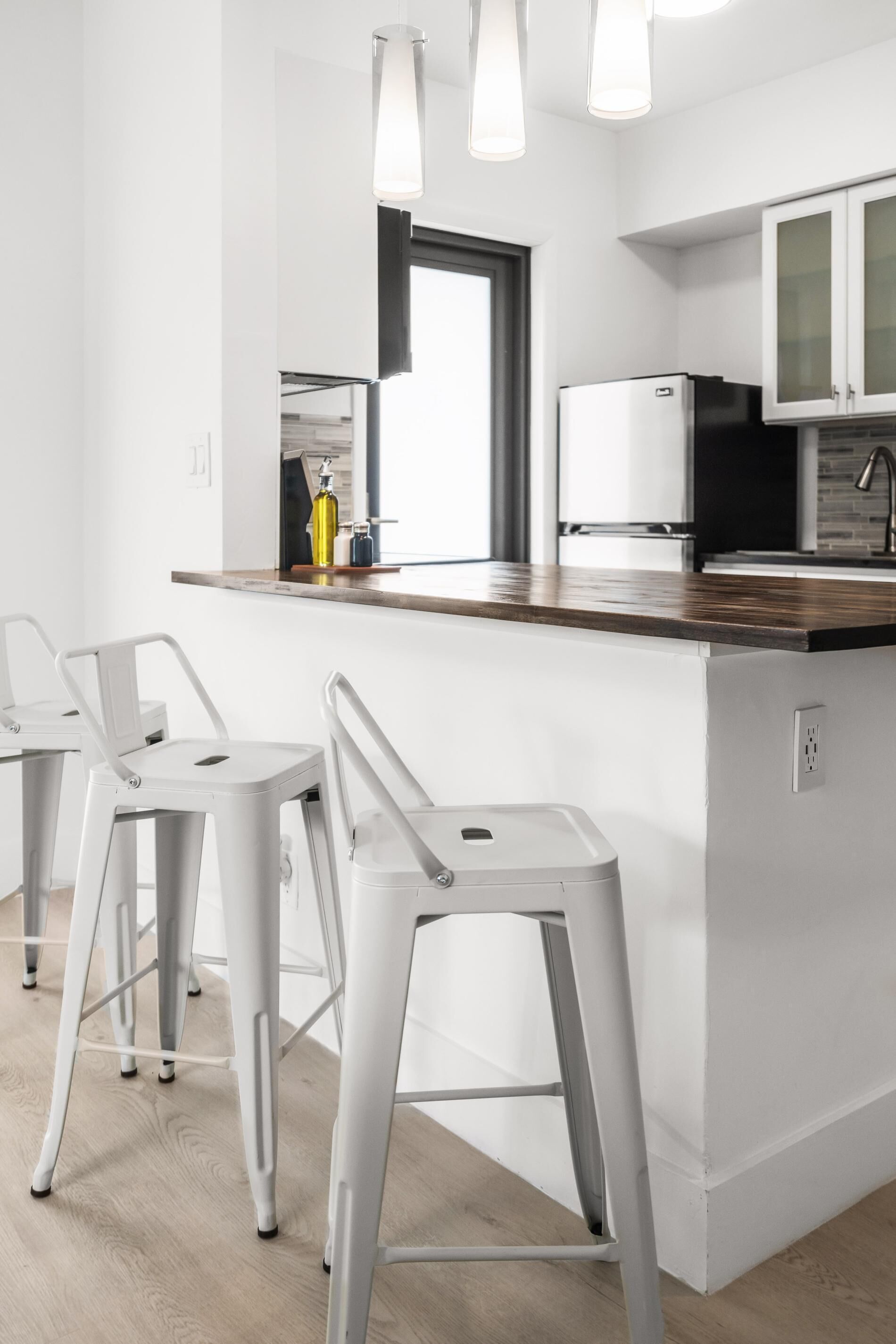 Una cucina moderna con sgabelli da bar bianchi, un piano di lavoro in legno e un frigorifero integrato.