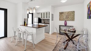 A modern kitchen with white cabinets, a wooden island, and a dining area with clear chairs and a glass table. - Modern 2/1 rent near Las Olas Fort Lauderdale (Fort Lauderdale)