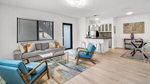 A modern living room with a grey sofa, blue armchairs, and a coffee table. A kitchen with white cabinets and a dining area with a table and chairs is visible in the background. - Modern 2/1 rent near Las Olas Fort Lauderdale (Fort Lauderdale)