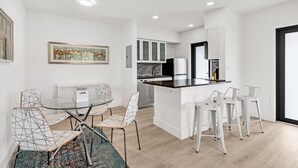 A modern kitchen with white cabinets, a black refrigerator, and a wooden countertop. There is a dining area with a glass table and wireframe chairs. - Rent 2/1 in Fort Lauderdale near Las Olas (Fort Lauderdale)