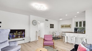 A modern living room with a cityscape view, a dining area with white furniture, and a kitchen with white cabinets and a bar. - Rent 2/1 in Fort Lauderdale near Las Olas (Fort Lauderdale)