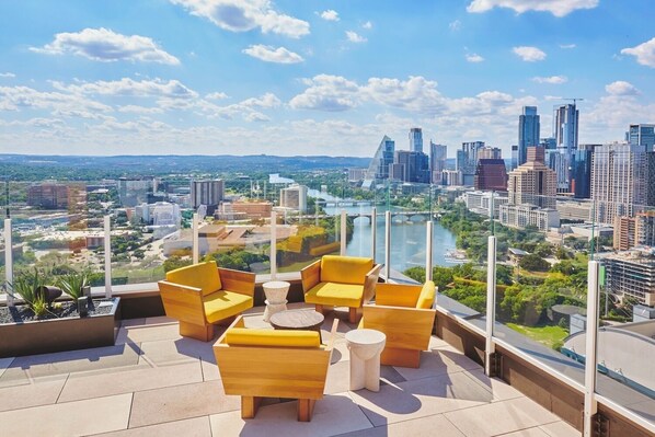 A rooftop terrace with yellow furniture, a view of a city skyline, and a river.
