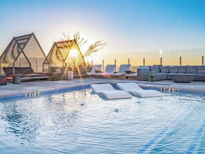 A pool area with lounge chairs, a hot tub, and a sunset view.