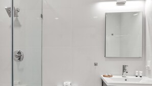 Een moderne badkamer met een douchecabine van glas, een toilet, een wastafel met spiegel en een afvalbak.
