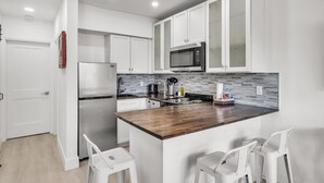 Een moderne keuken met witte kastjes, een roestvrijstalen koelkast, een magnetron en een houten kookeiland met barkrukken.