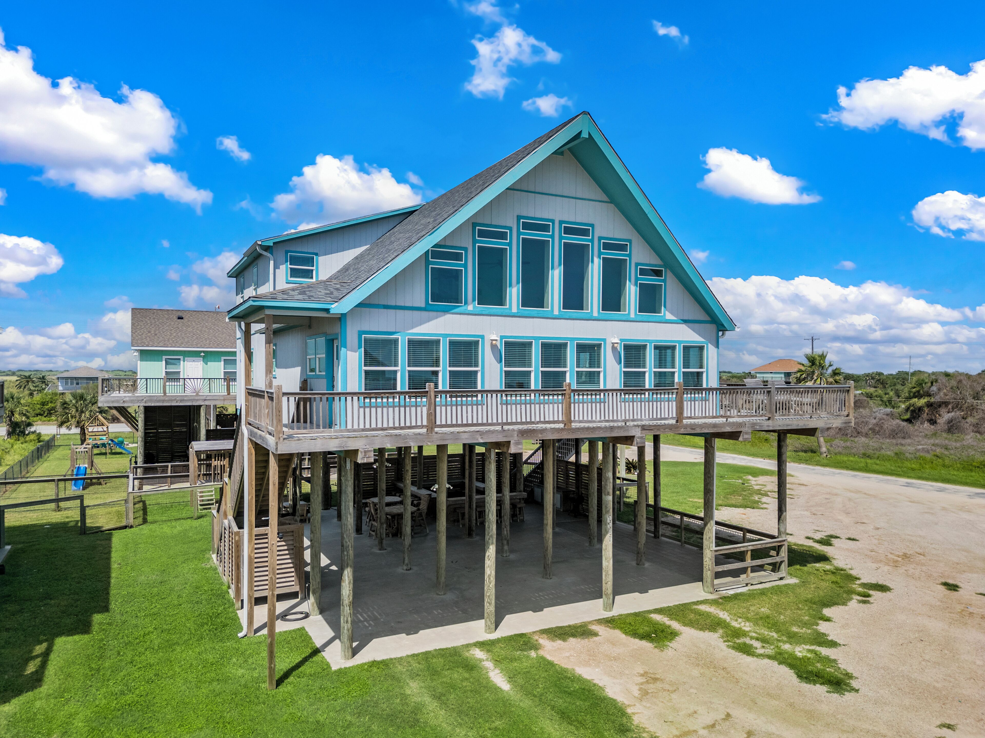 A two-story house with a balcony and a deck, surrounded by a grassy yard and a clear blue sky.