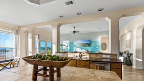 A spacious kitchen with a large island, a dining area with a wooden table, and a view of the ocean. - Spacious Getaway | Gulf Views & Gameroom Fun (Gilchrist)
