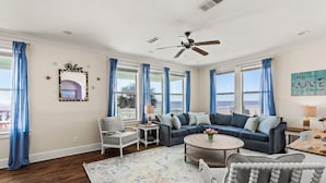A spacious living room with a blue sofa, a white armchair, a coffee table, and a ceiling fan. - Beachfront | Direct Access, Outdoor Bar & Grill (Crystal Beach)