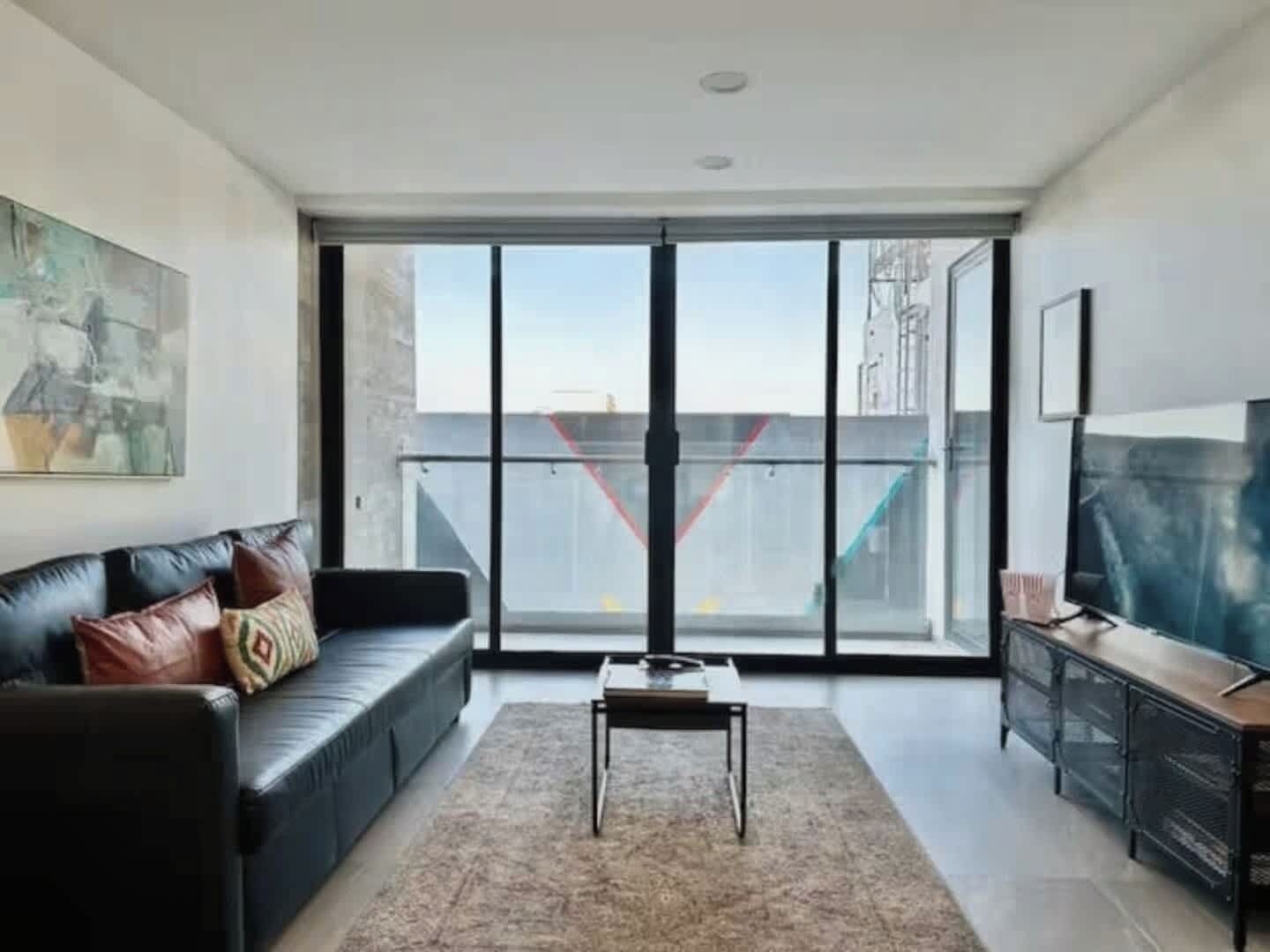 Uma sala de estar moderna com um sofá de couro preto, uma mesa de centro e uma TV em um armário de madeira.