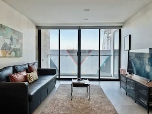 A modern living room with a black leather sofa, a coffee table, and a TV on a wooden cabinet. - Distrito Revolución 1 BR Suite 2nd Floor (Tijuana)