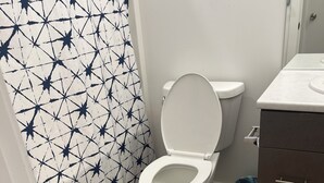 A modern bathroom with a white toilet, a patterned shower curtain, a wooden floor, and a dark-colored rug. - Modern & Central 3BED/2BATH near Health Science Center (Winnipeg)