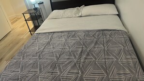 A neatly made bed with a patterned bedspread, a bedside table with a lamp, and a small heater on the floor. - Modern & Central 3BED/2BATH near Health Science Center (Winnipeg)