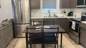 A modern kitchen with stainless steel appliances, a dining table with chairs, and a window with blinds. - Modern & Central 3BED/2BATH near Health Science Center (Winnipeg)