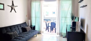 A living room with a dark sofa, a starfish decoration, a lamp, and a view of the outside.