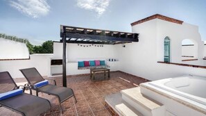 Una terrazza sul tetto con una pergola, una zona salotto con cuscini, una vasca idromassaggio e un pavimento piastrellato.