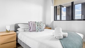 Una cama bien hecha con ropa de cama blanca, una manta verde y una ventana con persianas.