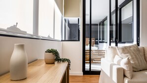 Una sala moderna con un sofá, una mesa de madera con un jarrón y una planta, y vistas a una escalera que lleva a otra habitación.