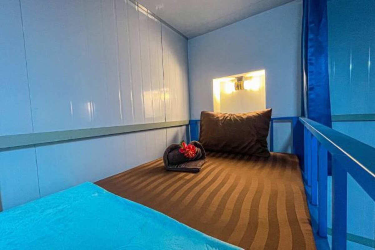 Ein kleiner, gemütlicher Raum mit einem Einzelbett, einem Nachttisch mit Lampe und einem Fenster mit Vorhängen.