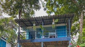 Ein zweistöckiges Gebäude mit Balkon, umgeben von üppiger Vegetation und blühenden Pflanzen.