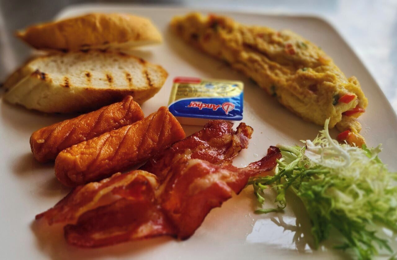 Une assiette de petit-déjeuner comprenant du poulet grillé, du bacon, des œufs brouillés, des toasts et une salade en accompagnement.