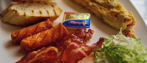 Une assiette de petit-déjeuner comprenant du poulet grillé, du bacon, des œufs brouillés, des toasts et une salade en accompagnement.