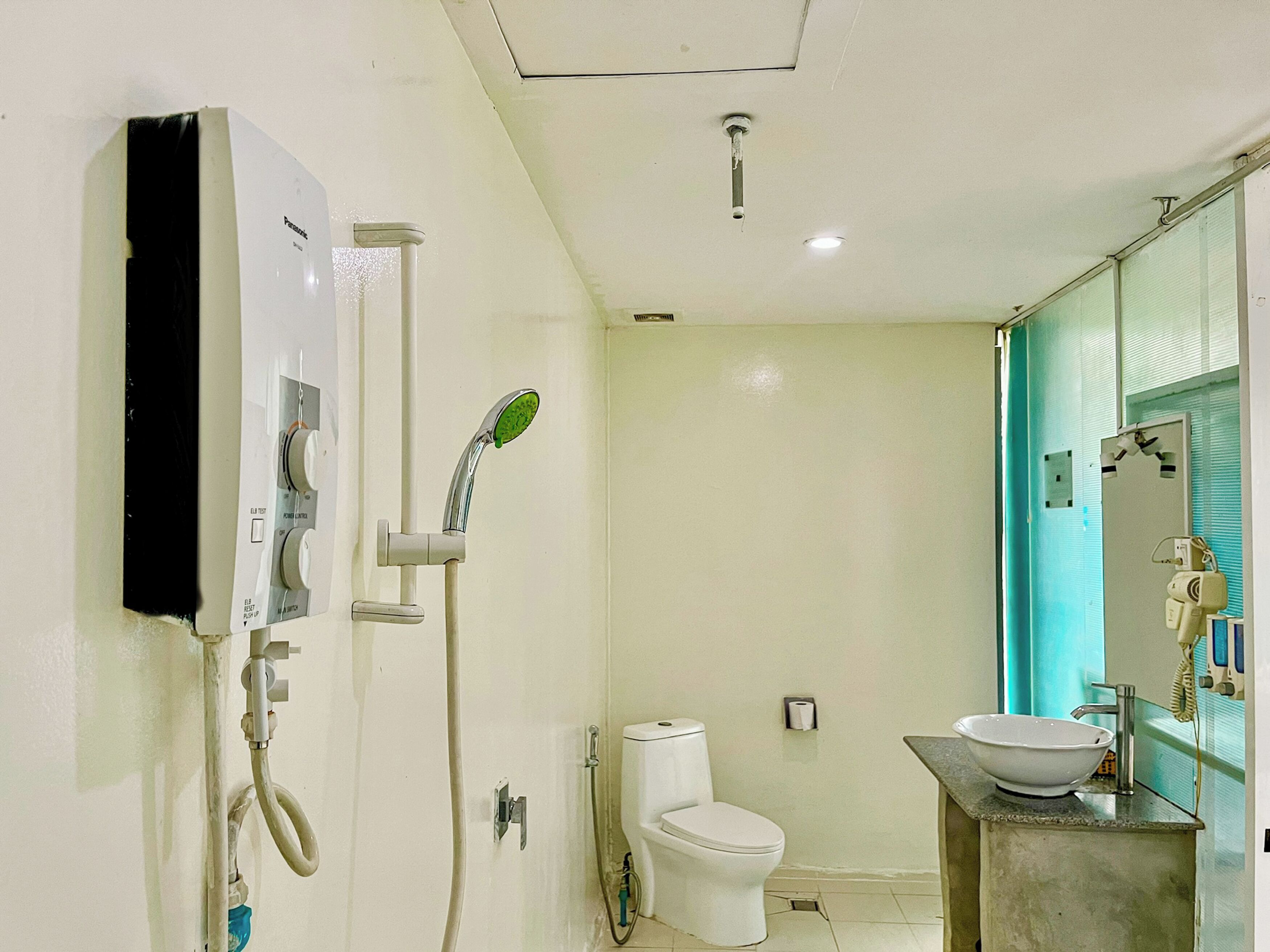 A bathroom with a toilet, a sink, a shower with a control panel, and a mirror with a towel rack.