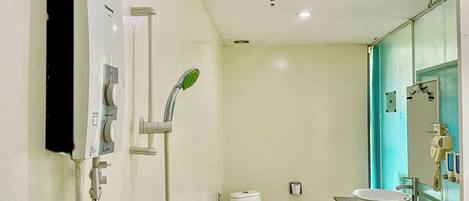 A bathroom with a toilet, a sink, a shower with a control panel, and a mirror with a towel rack.