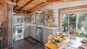 A kitchen with wooden beams, a stove, and a dining area with a table set for two. - Relax. Soak. Explore. Repeat. | Bella Luna Cabin (Ruidoso)