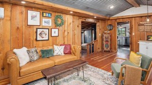 A cozy cabin interior with a wooden wall, a sofa, a coffee table, and a dining area. - Relax. Soak. Explore. Repeat. | Bella Luna Cabin (Ruidoso)