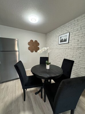 Un comedor con una mesa redonda, cuatro sillas, una planta en maceta, un adorno en la pared y un cuadro enmarcado.