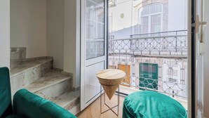 Ein Balkon mit schmiedeeisernem Geländer, einem Holztisch und einem grünen Stuhl.