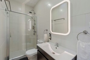 Une salle de bain moderne avec une douche à parois de verre, des toilettes blanches, un meuble-lavabo avec un miroir et un porte-serviettes.