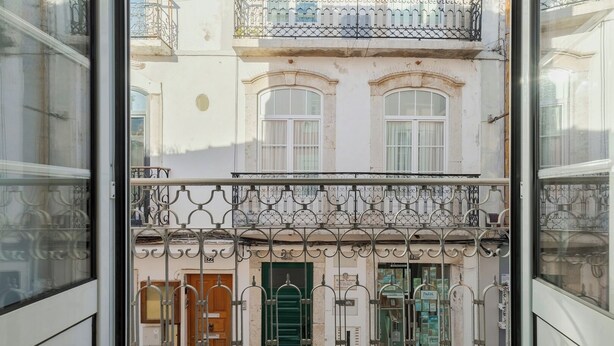 Ein Balkon mit schmiedeeisernen Geländern, Blick auf ein Gebäude mit Rundbogenfenstern und eine Tür mit grünem Rollo.