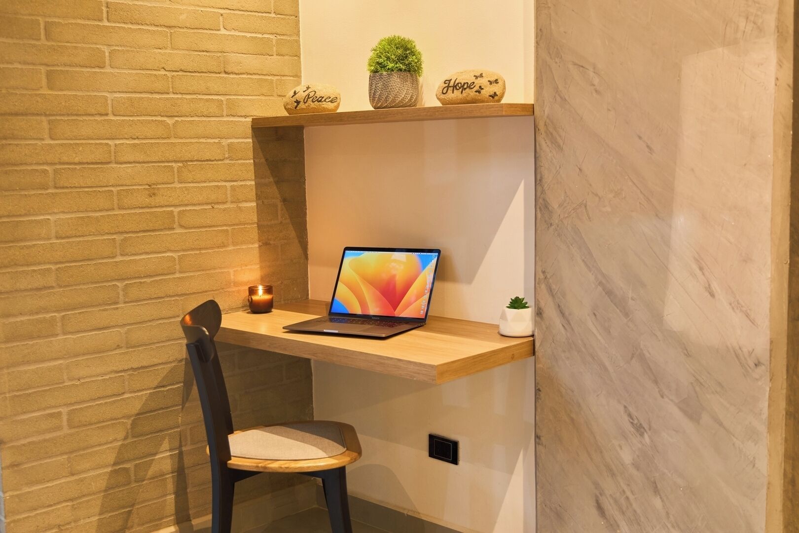 Un'area dedicata al lavoro, con un portatile su una scrivania in legno, una sedia, una candela e oggetti decorativi su uno scaffale.