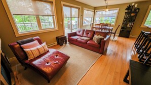 A spacious living room with a red leather sofa, a dining area with a table and chairs, and large windows providing natural light. - 2-bedroom condo with hot tub and mountain views (Golden)