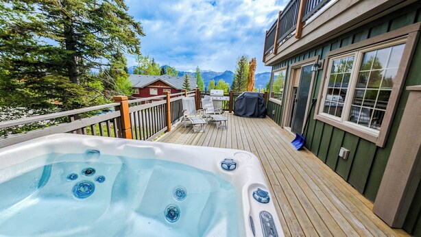 A hot tub on a wooden deck with a view of mountains and a house in the background. - 2-bedroom condo with hot tub and mountain views (Golden)