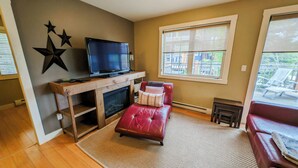 A living room with a fireplace, a television, and a red leather sofa. - 2-bedroom condo with hot tub and mountain views (Golden)