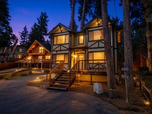 A two-story lodge with a staircase leading to the entrance, surrounded by trees.