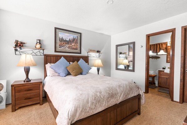 A bedroom with a wooden bed, two bedside tables with lamps, a wall-mounted mirror, and a framed picture above the bed.