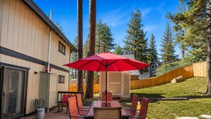 A deck with a table and chairs, a red umbrella, and a wooden fence. - Mama Bear's Cottage - Portable AC, Close to Slopes, Fenced Yard, Pet Friendly (Big Bear Lake)
